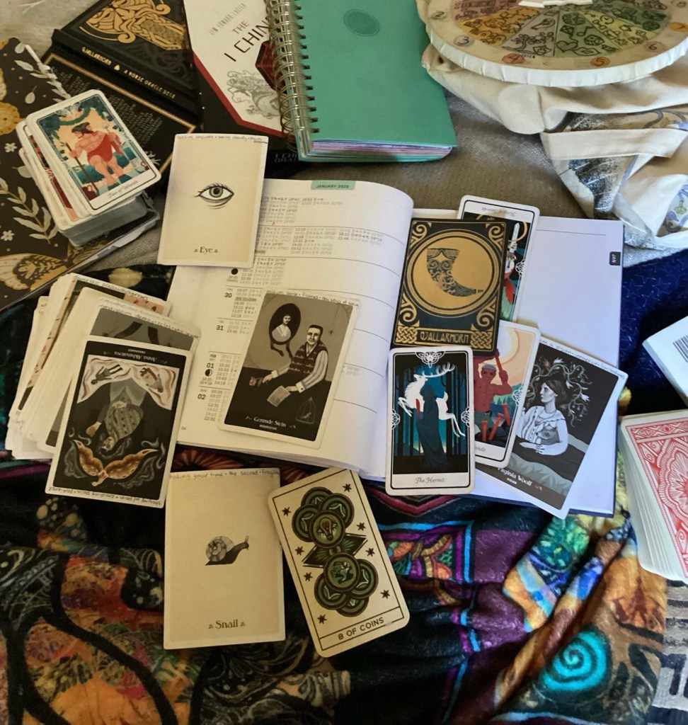 an assortment of oracle and tarot cards spread over an astrological ephemeris in regards to the oracle message written